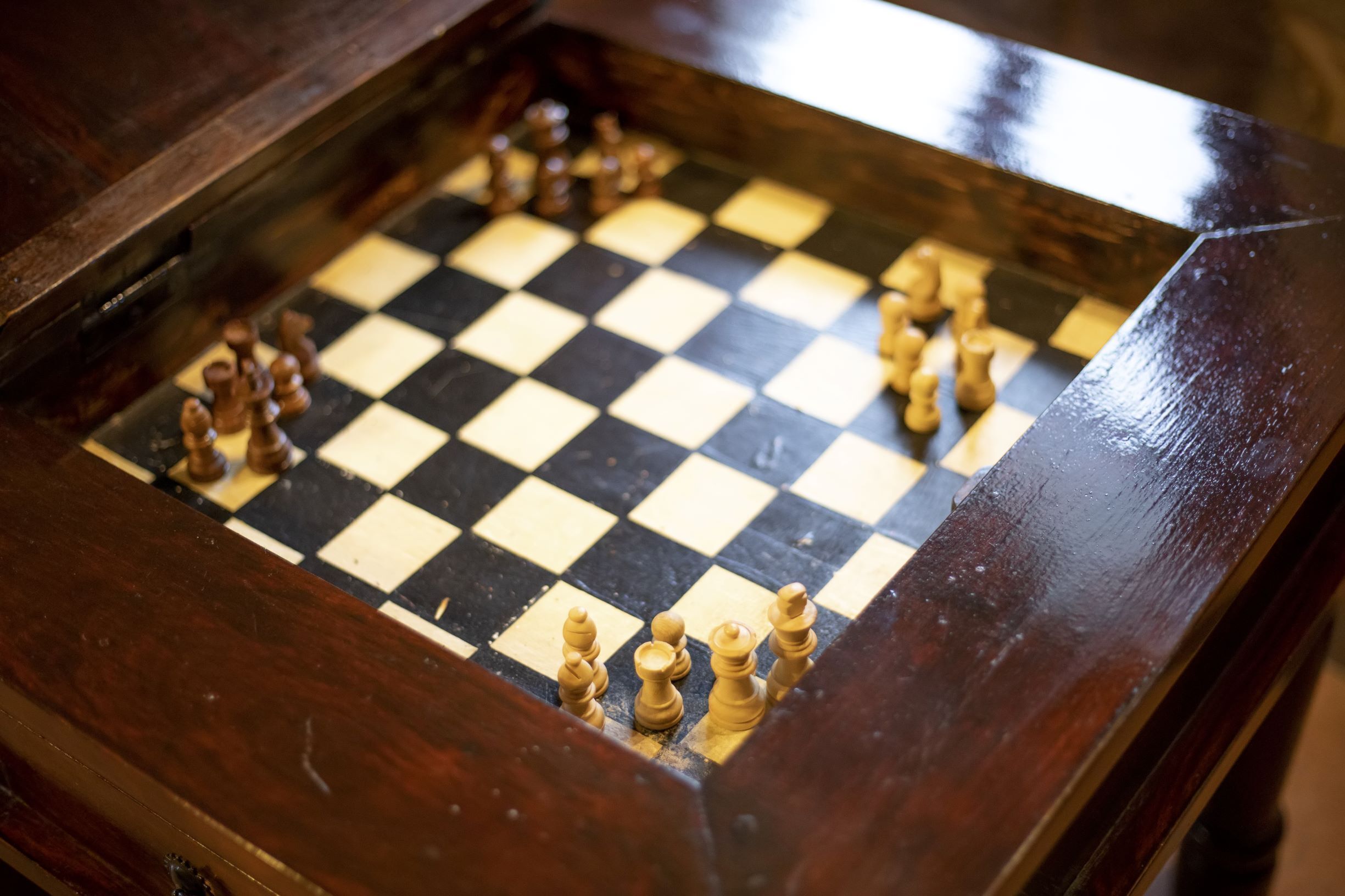 Een detail van een houten schaak tafel met een geruit bord en schaakstukken.