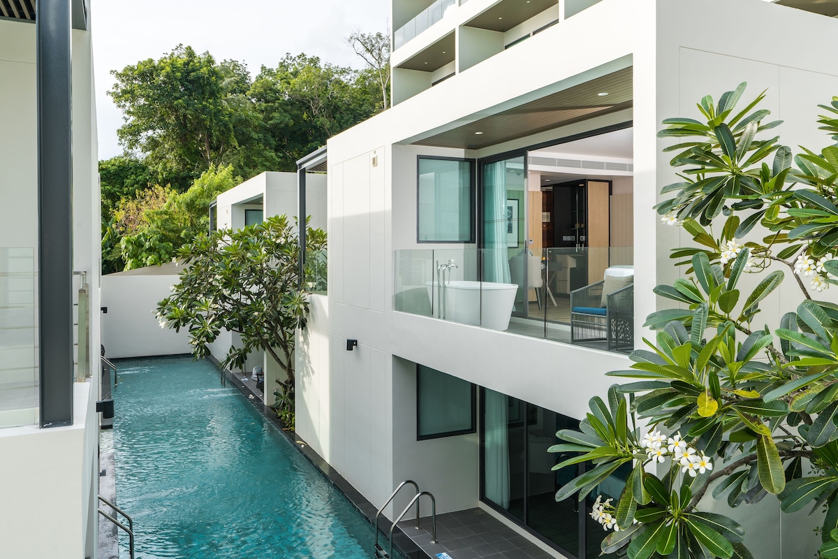 Un bâtiment moderne doté d’une piscine, de grandes fenêtres et d’une végétation luxuriante.