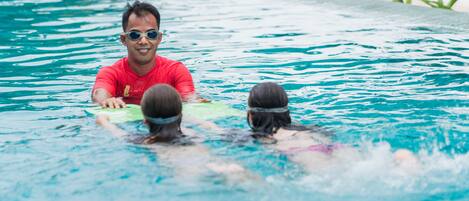 A swimming pool with clear blue water, a person in a red shirt, and another in a pink swimsuit.