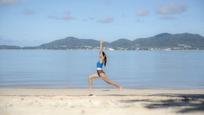 A person performing a yoga pose on a beach with a clear sky and mountains in the background. - My Beach Resort Phuket (Wichit)
