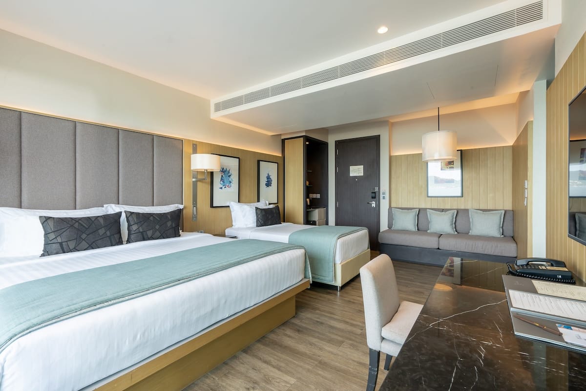 Une chambre d’hôtel avec deux lits, un canapé, un bureau avec une chaise et une grande fenêtre.