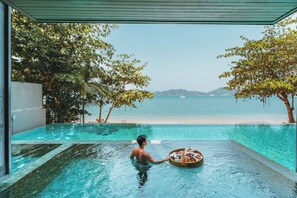 Un hombre en una piscina con una bandeja de comida, con vista a una playa y al océano.