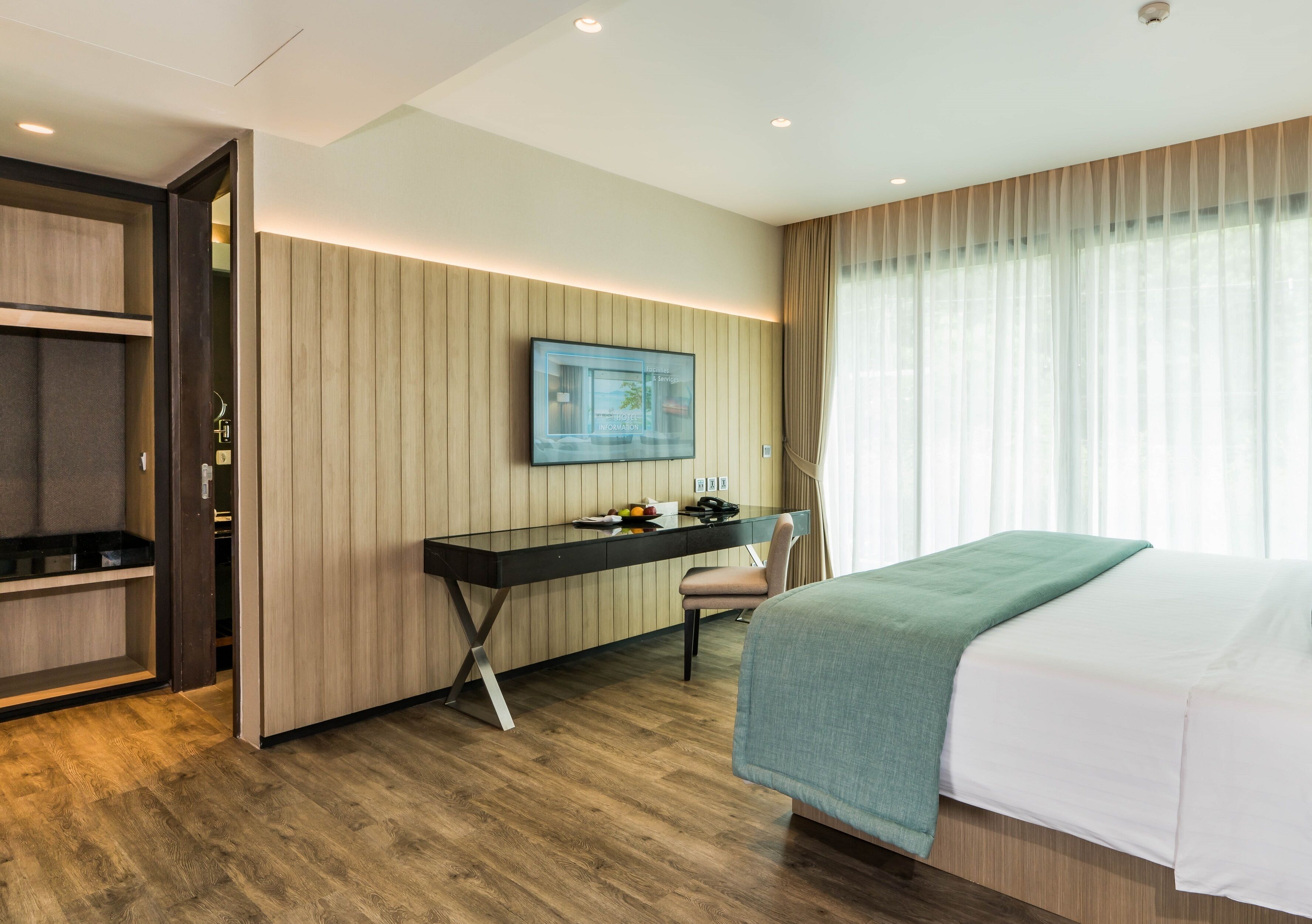 Ein Hotelzimmer mit Bett, Schreibtisch mit Stuhl, Fernseher und Kleiderschrank.