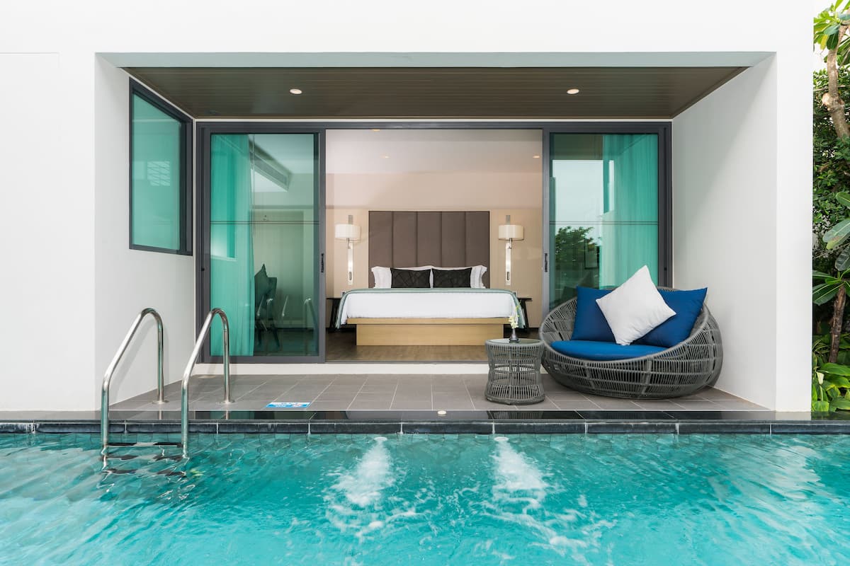 Une chambre d’hôtel moderne dotée d’une porte en verre donnant sur une chambre à coucher, d’un espace de détente près de la piscine et d’une salle de bain visible.