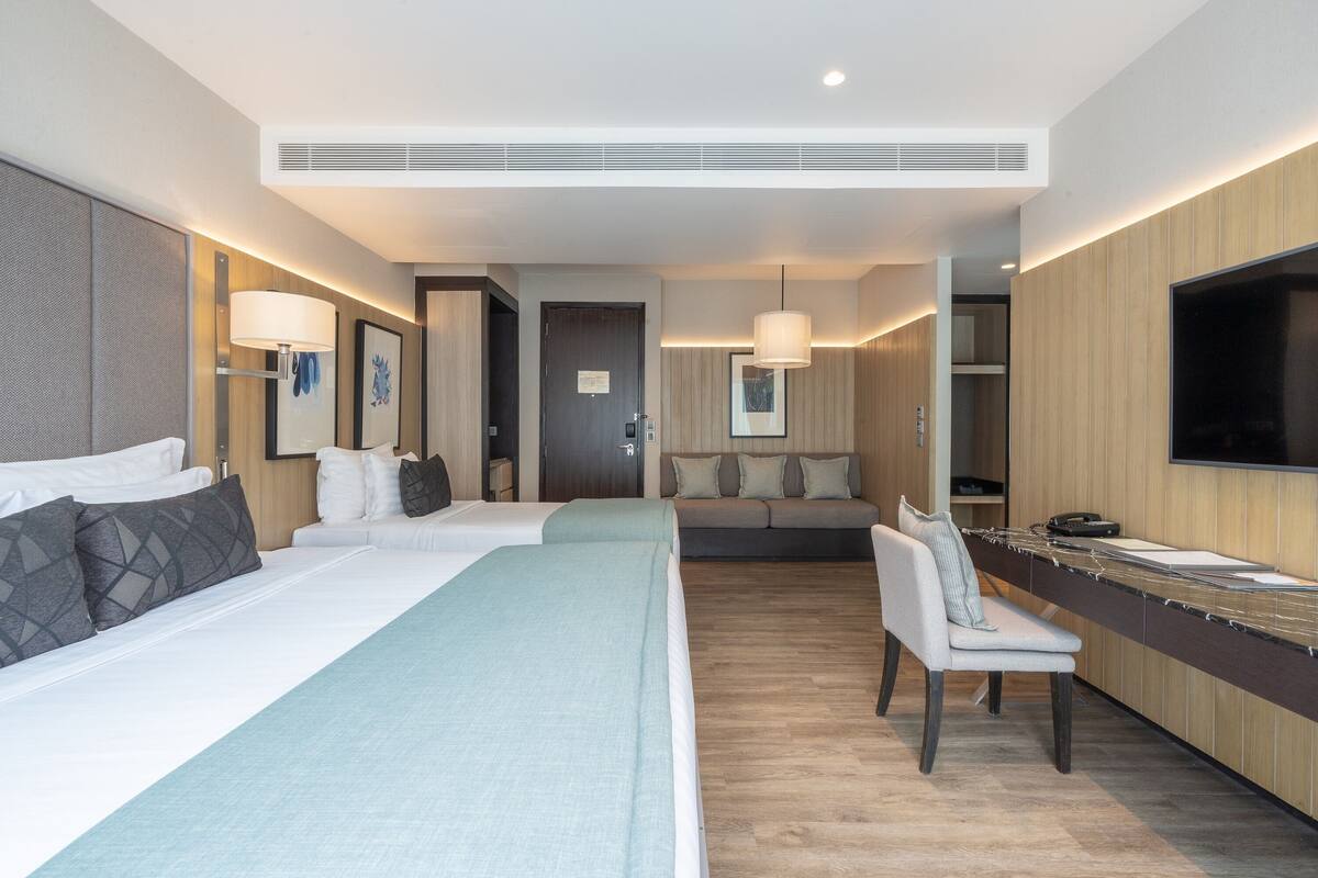 Une chambre d’hôtel avec deux lits, un bureau, une chaise, une télévision et un canapé.