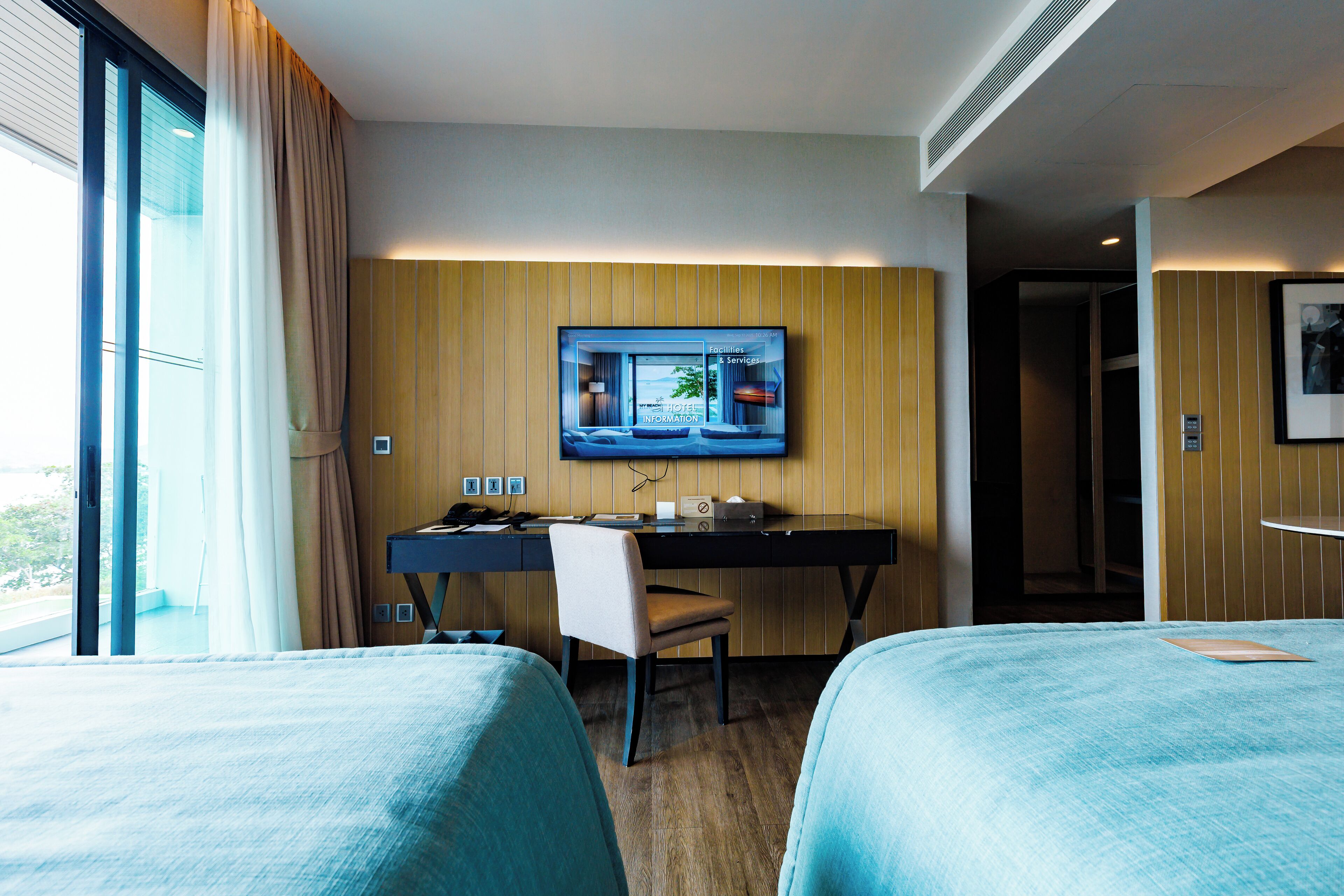 A hotel room with a desk, two beds, a television, and a window with curtains.