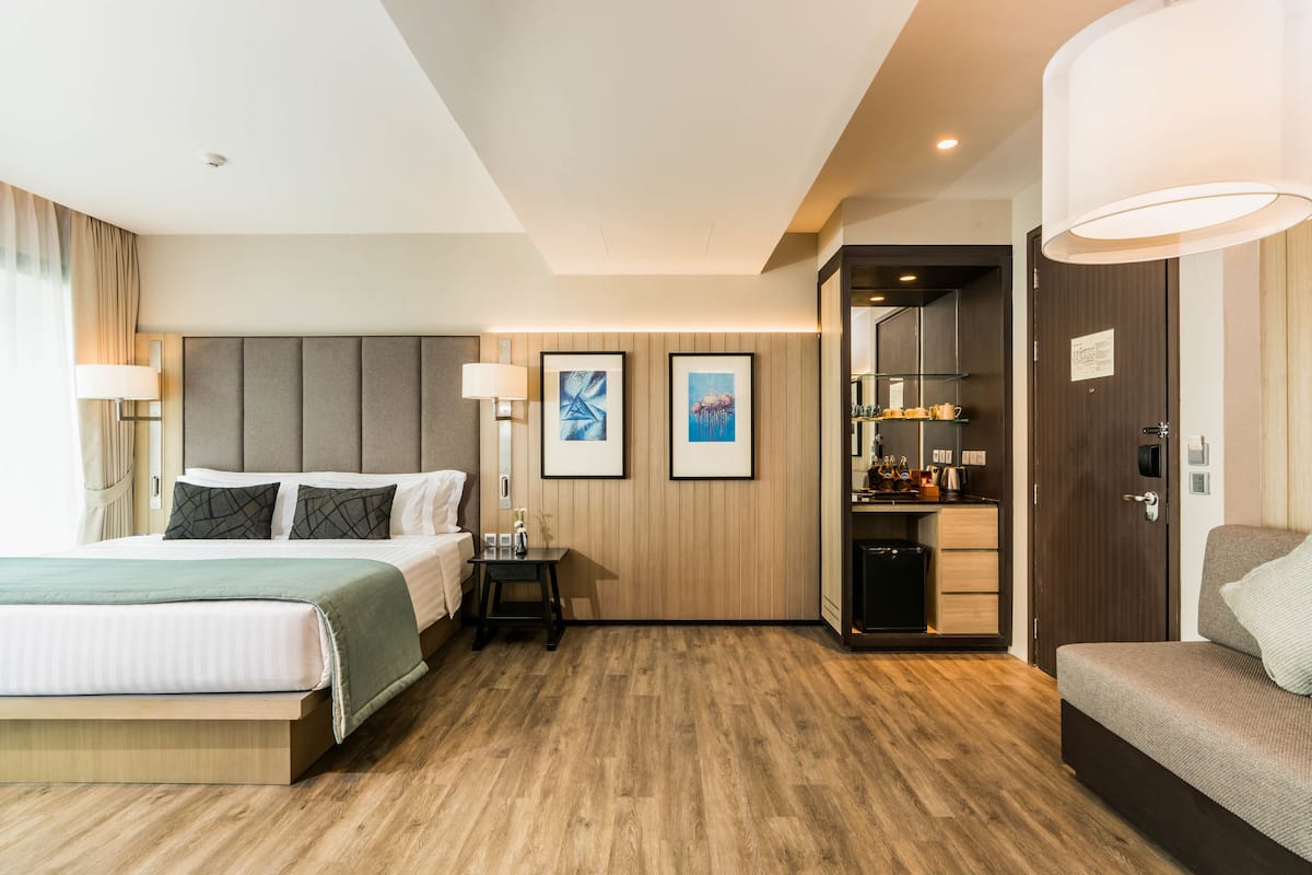 Une chambre d’hôtel moderne avec un grand lit, un canapé, un bureau avec une lampe et une petite kitchenette.