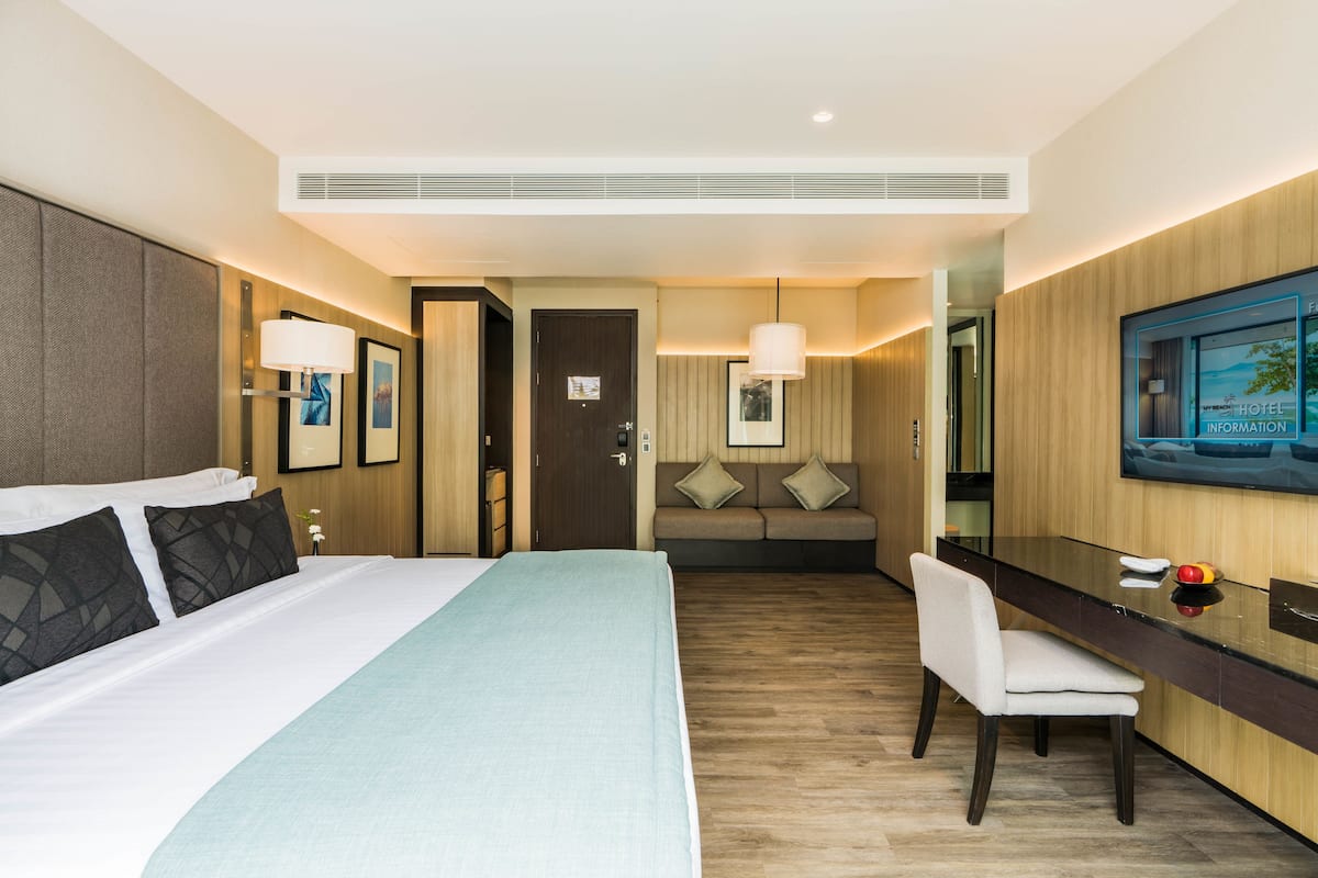 Une chambre d’hôtel avec un grand lit, un bureau, une chaise, un canapé et un téléviseur fixé au mur.