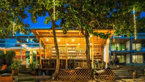 Un edificio frente a la playa con una terraza de madera, plantas en macetas y una valla.