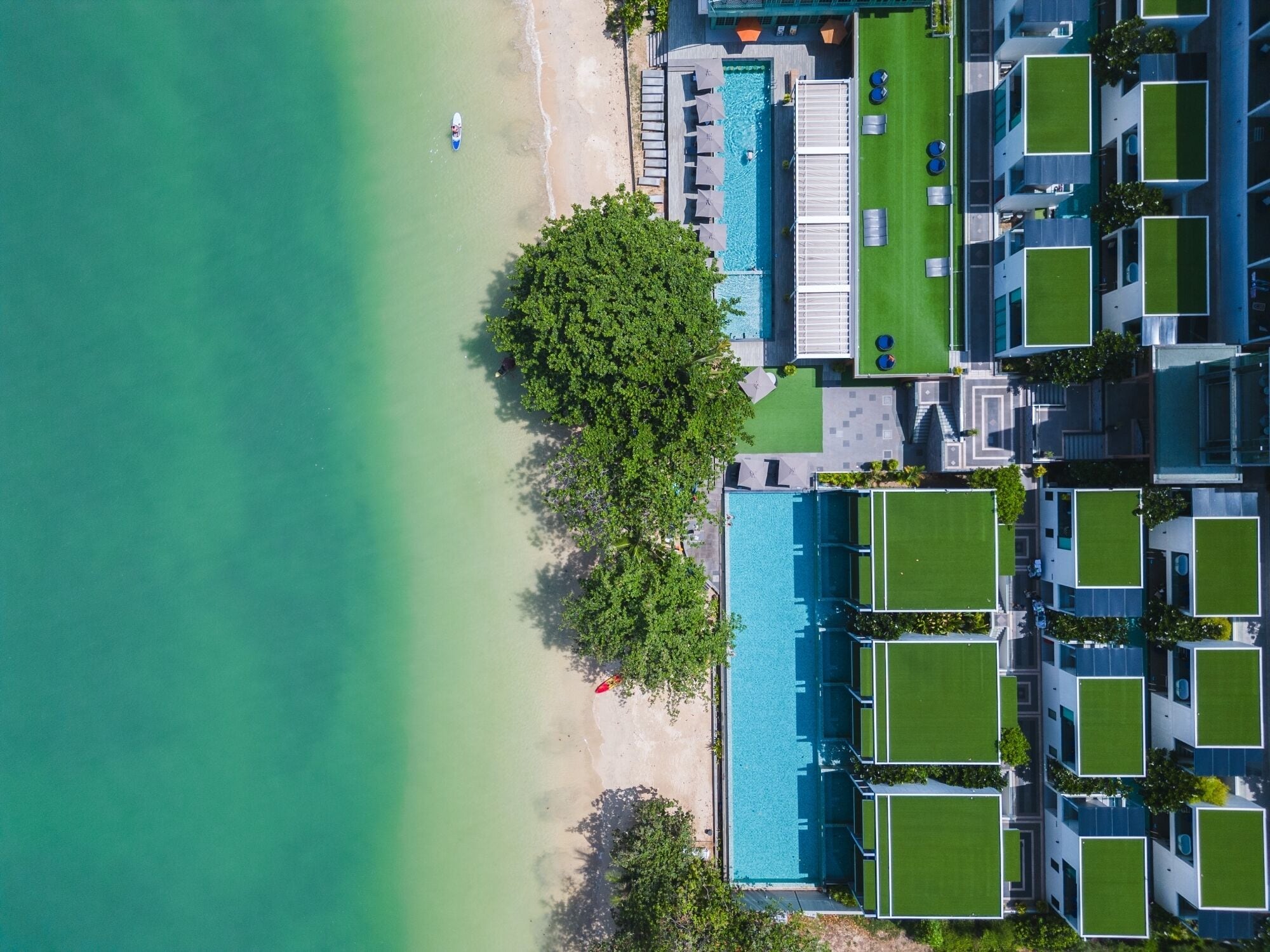An aerial view of a resort with a swimming pool, beach, and modern buildings.