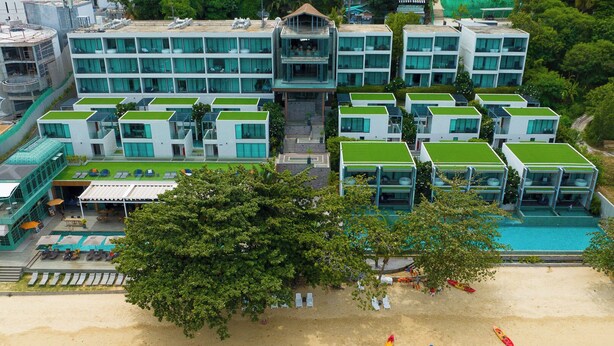 Un hotel frente a la playa con edificios de varios pisos, piscina y una playa de arena.