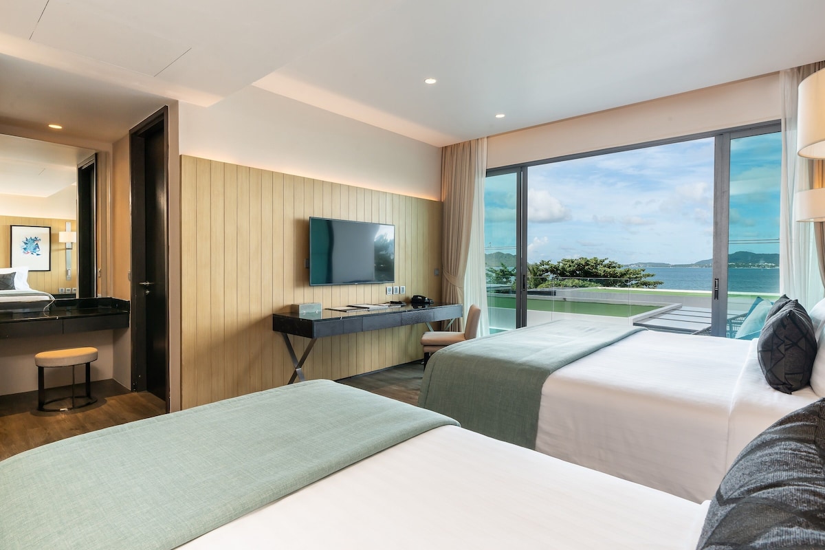 Une chambre d’hôtel avec deux lits, un bureau, une télévision et une vue sur la mer.