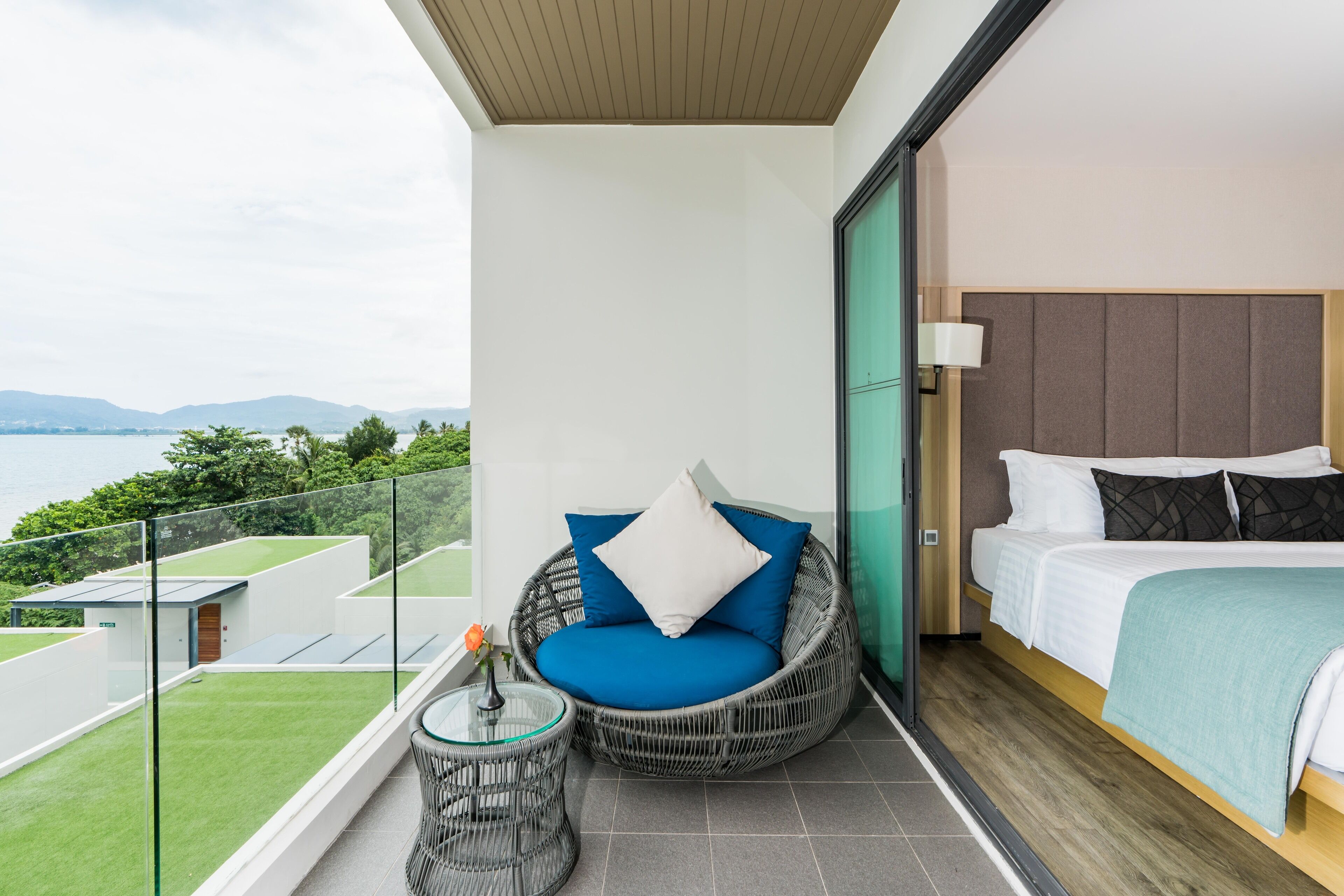 A balcony with a wicker chair, a small table with a vase, and a bed with a headboard.