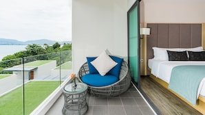 A balcony with a wicker chair, a small table with a vase, and a bed with a headboard. - My Beach Resort Phuket (Wichit)