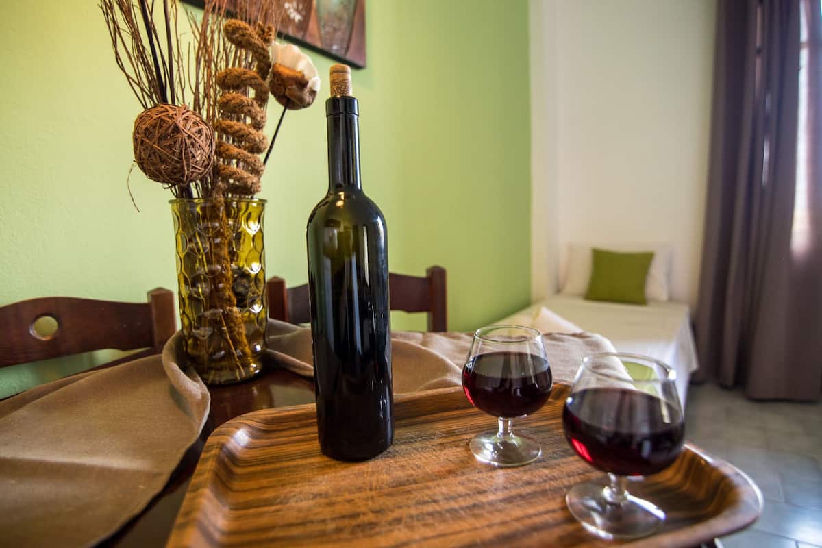 Una mesa de comedor con una botella de vino, dos copas de vino y un jarrón decorativo con plantas secas.