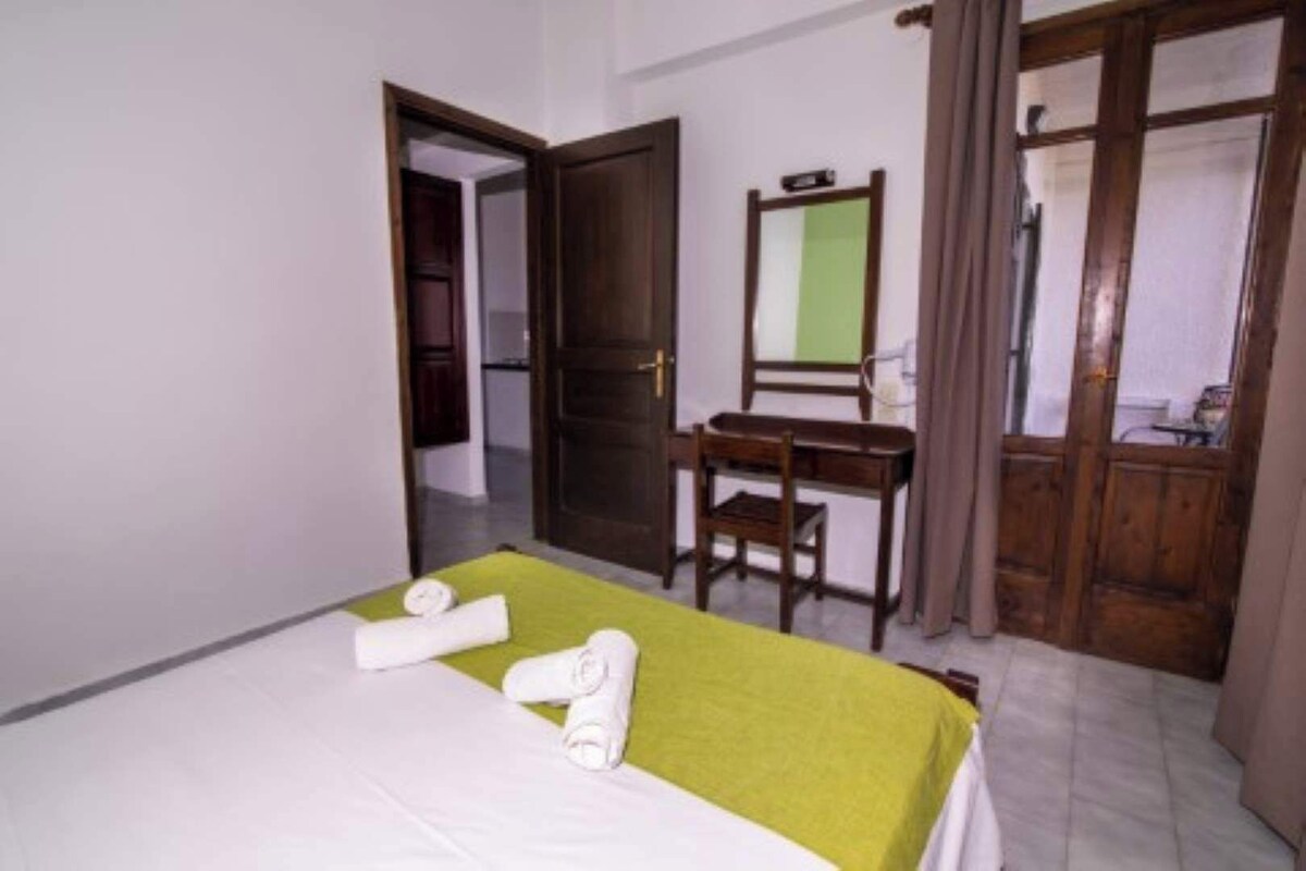 A hotel room with a bed, a desk, a chair, a mirror, and a wardrobe.