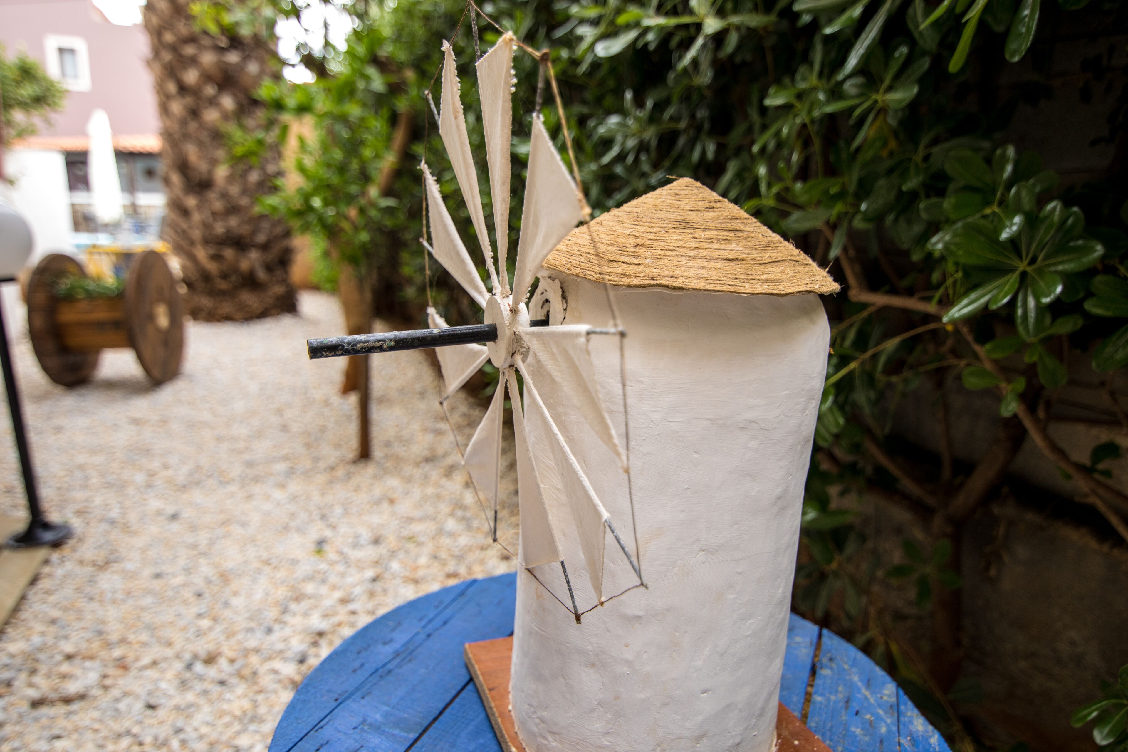 Un moulin à vent blanc, avec un toit en bois et un mât noir, posé sur une table bleue à l’extérieur.
