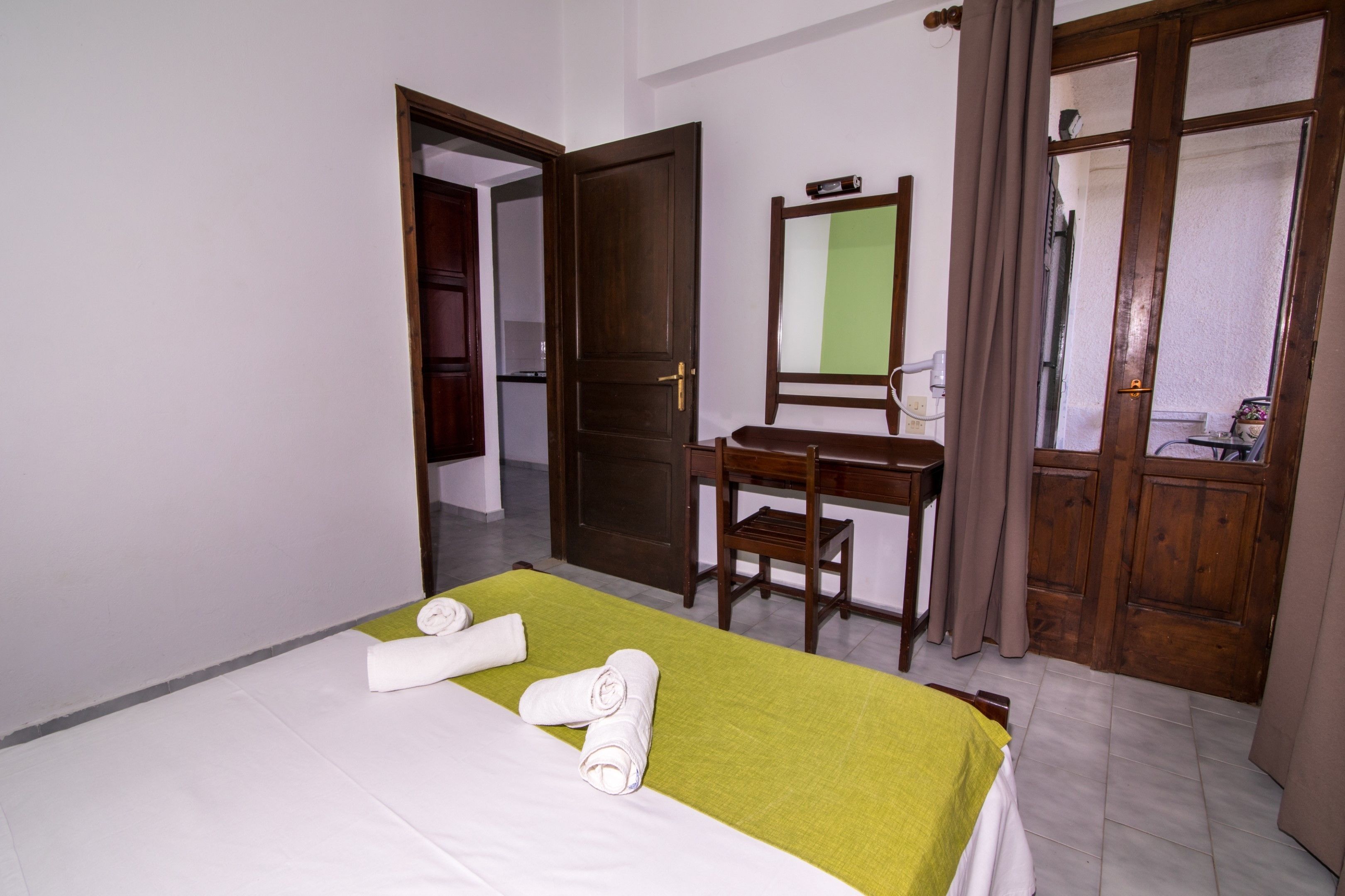 A hotel room with a bed, a desk, a chair, and a mirror.