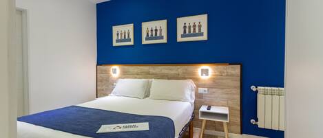 A hotel room with a large bed, a nightstand, a wall-mounted light, and a framed picture above the bed.