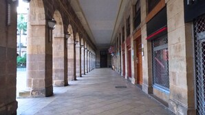 A corridor with stone columns and a tiled floor, leading to a building with a sign that reads "PAD". - Casual Blue (Bilbao)