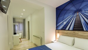 A hotel room with a bed, a desk, a chair, a radiator, and a wall with a blue escalator mural. - Casual Blue (Bilbao)