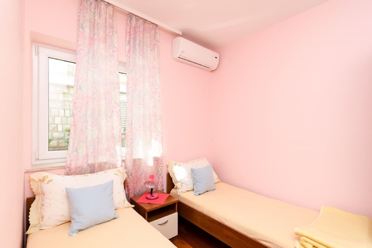 Quarto com duas camas, uma mesa de cabeceira, uma luminária e um ar condicionado.