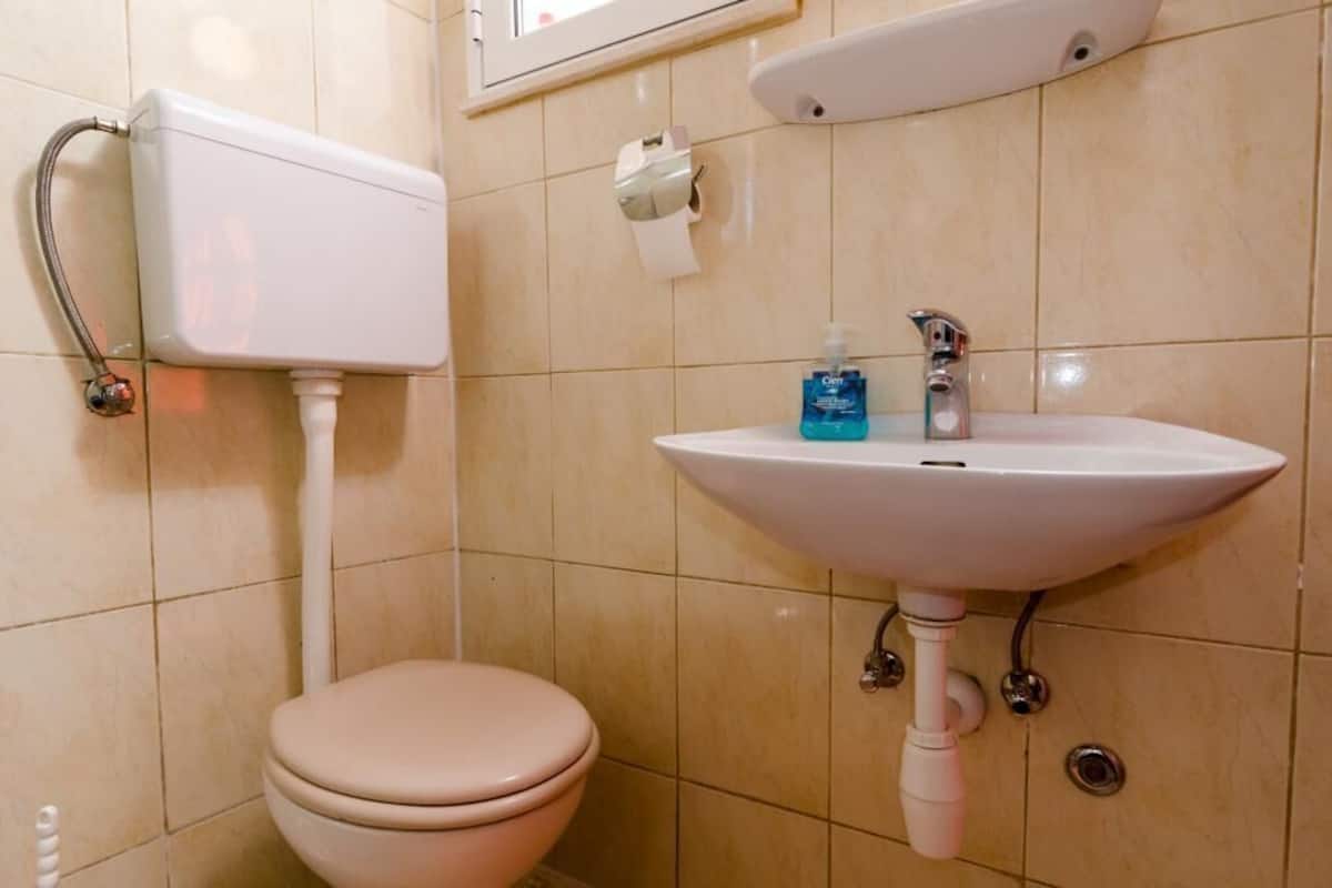Casa de banho com sanita, lavatório e suporte para papel higiénico.