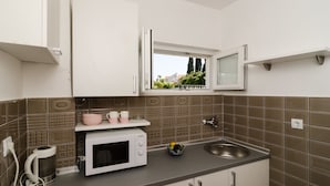 A compact kitchen with a microwave, sink, and window overlooking a garden. - Guest House Cuk (Dubrovnik)