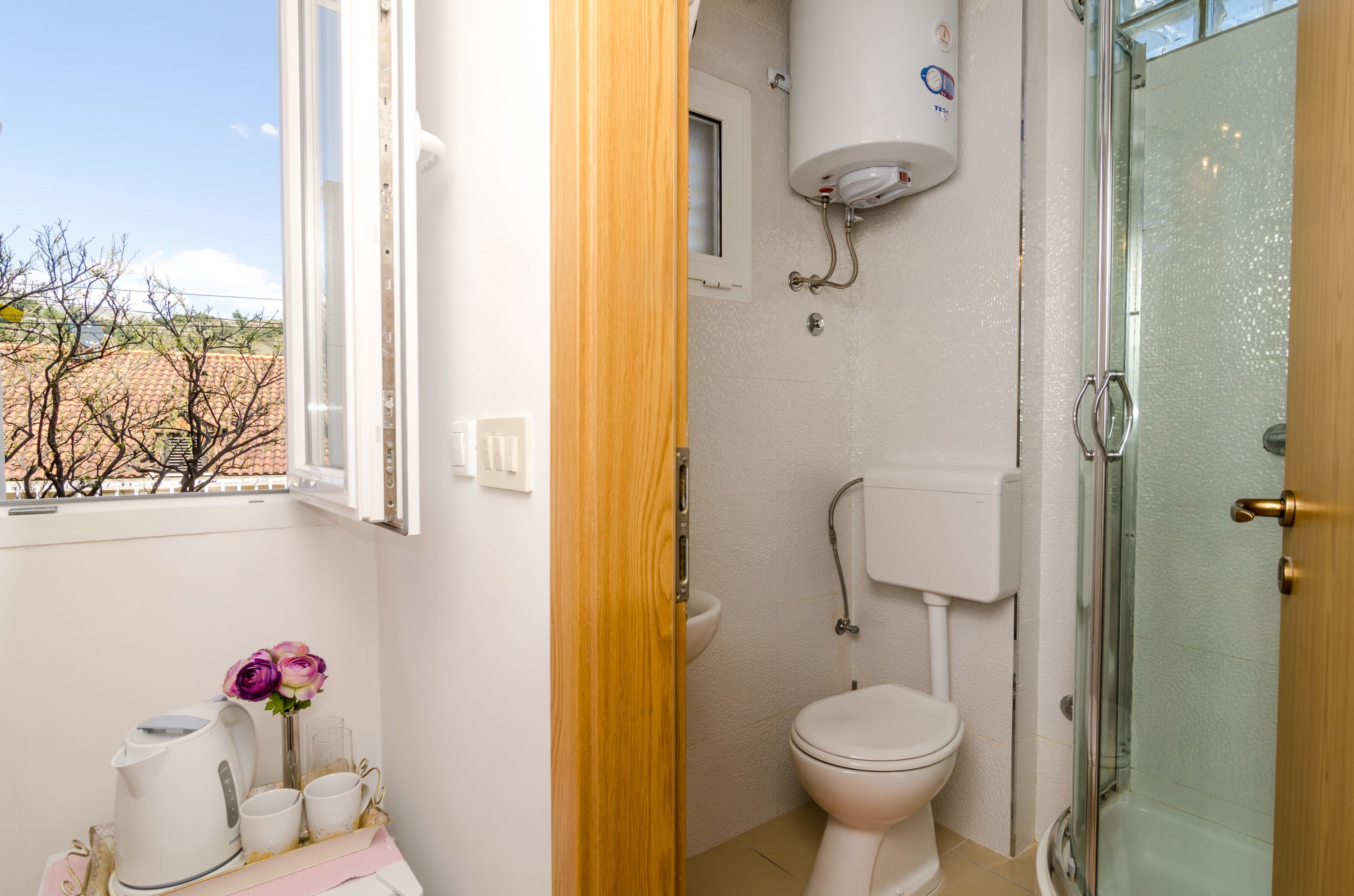 Un bagno con toilette, doccia e finestra vista alberi.