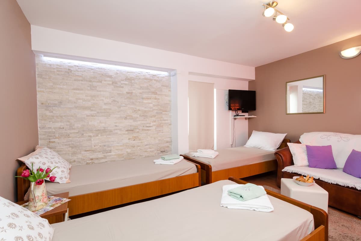 Quarto de hotel com duas camas de solteiro, um sofá, uma televisão e uma parede de pedra.