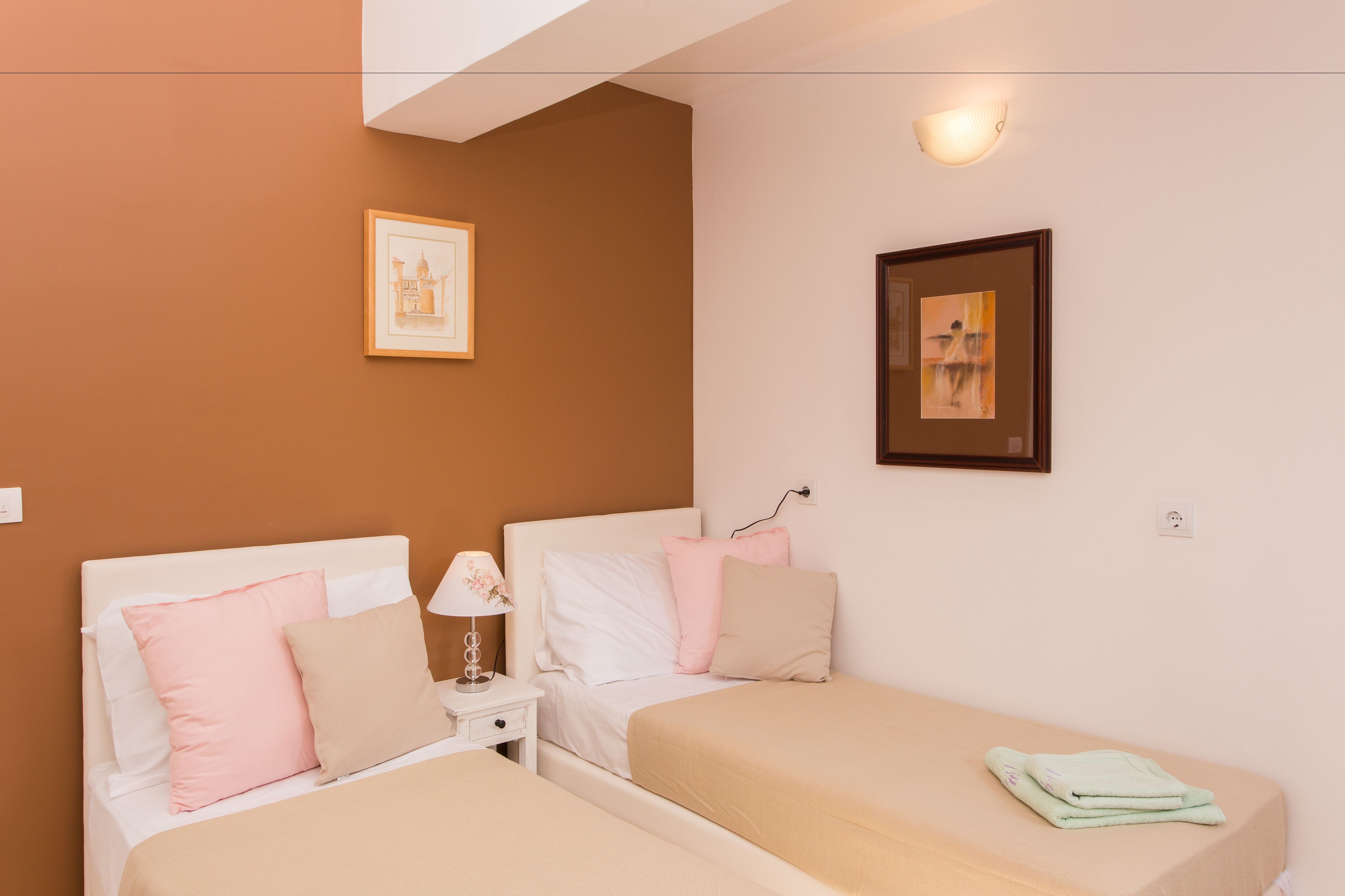 Un dormitorio con dos camas, una mesita de noche, una lámpara y dos cuadros en la pared.