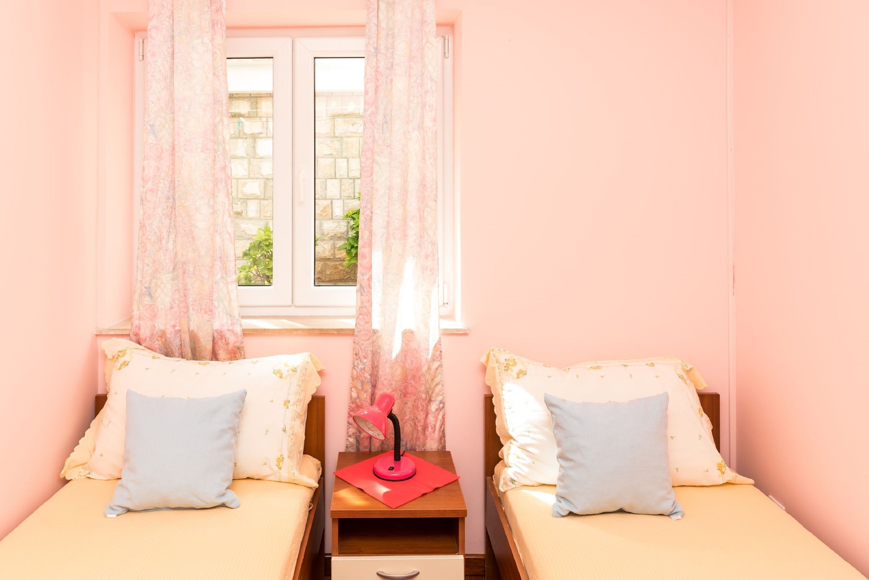 A bedroom with two single beds, a nightstand with a lamp, and a window with curtains.