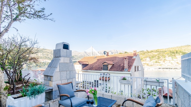 A terrace with outdoor seating, a stone fireplace, and a view of a coastal town. - Guest House Cuk (Dubrovnik)