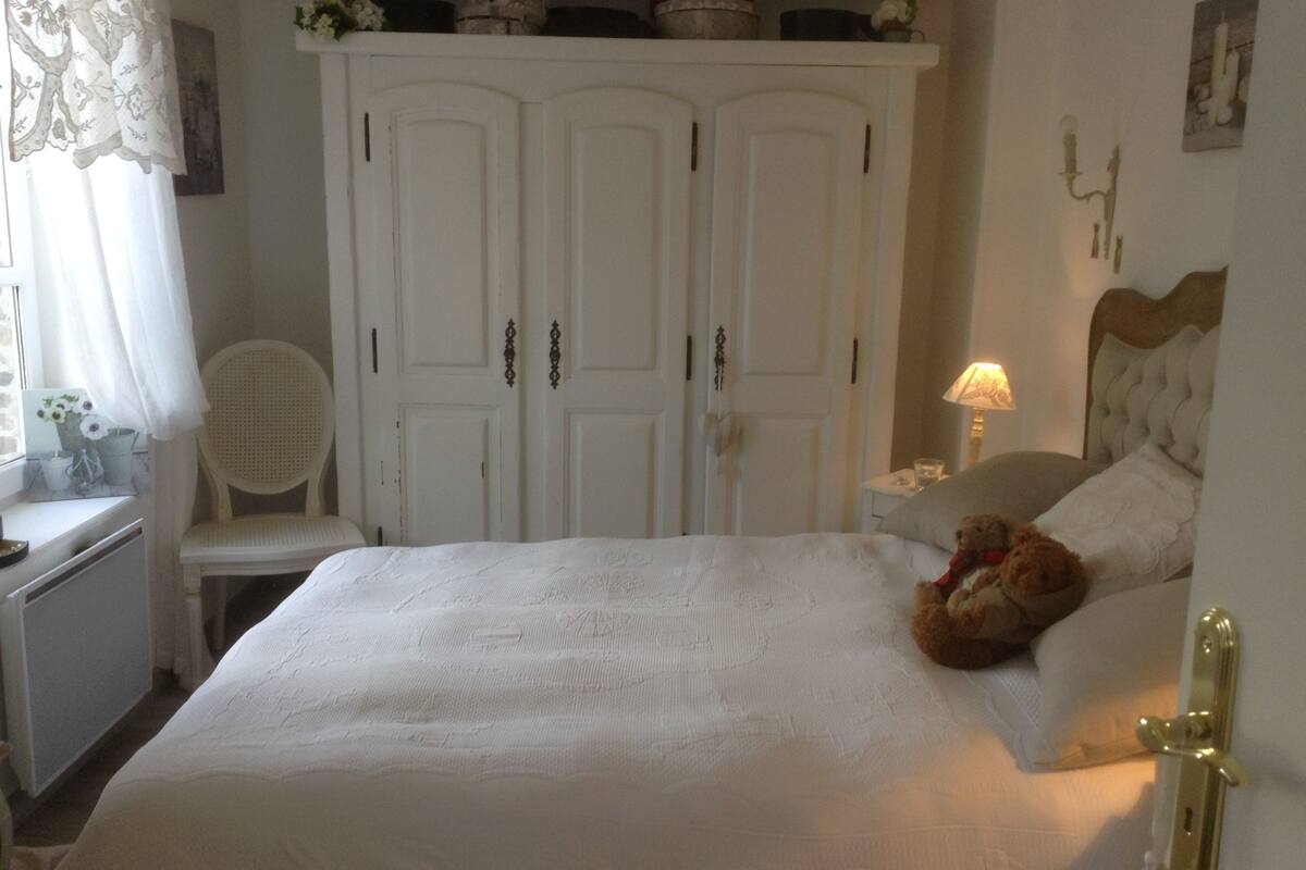Un dormitorio con una cama grande, una silla, un armario y una mesita de noche con lámpara.