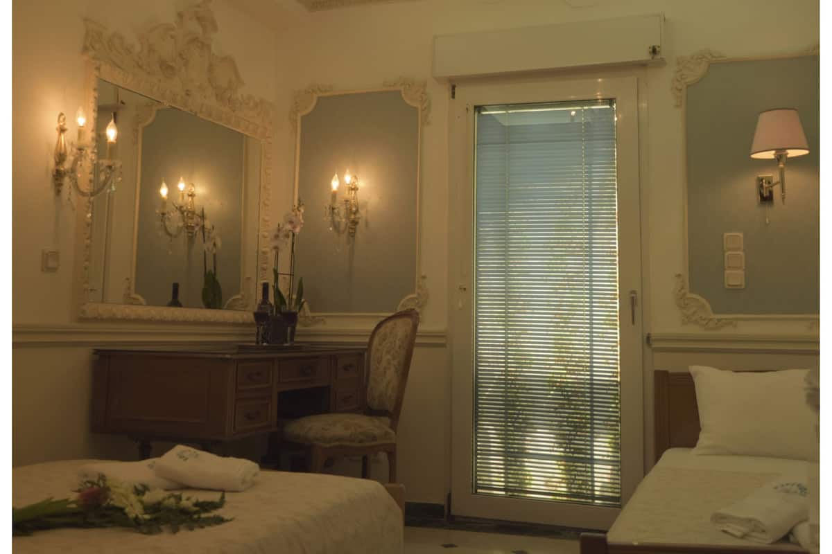 A hotel room with a large bed, a smaller bed, a vanity with a mirror, a chandelier, and a window with blinds.