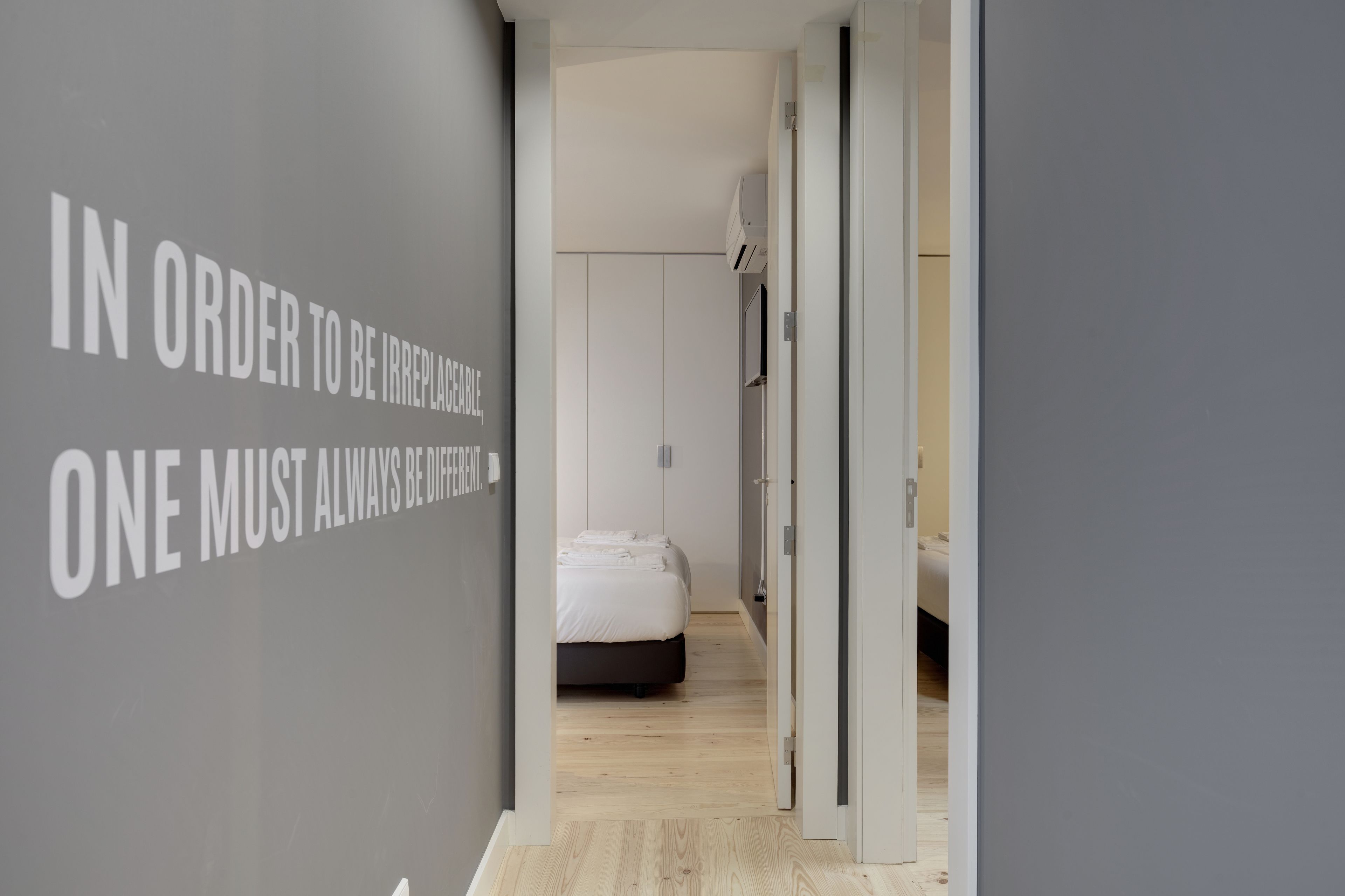 Un couloir menant à une chambre à coucher, où se trouvent un lit et un mur orné de texte.