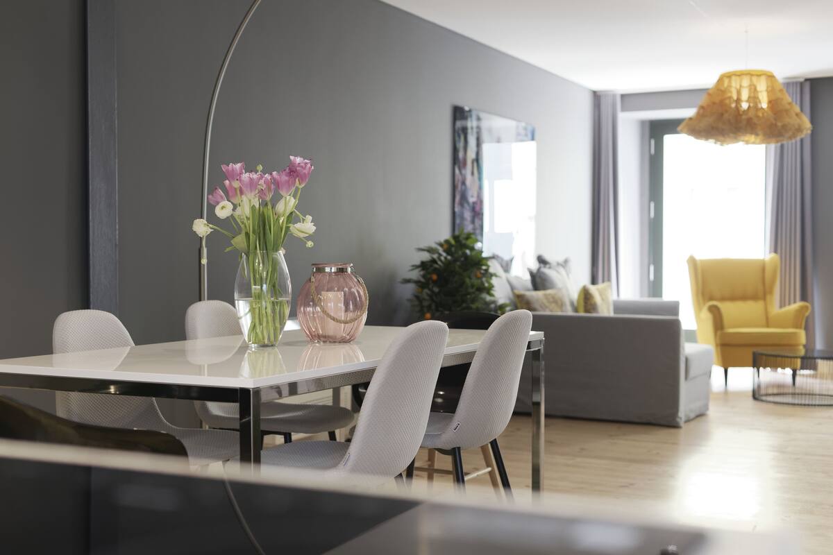 A modern dining area with a white table, grey chairs, and a vase with flowers.