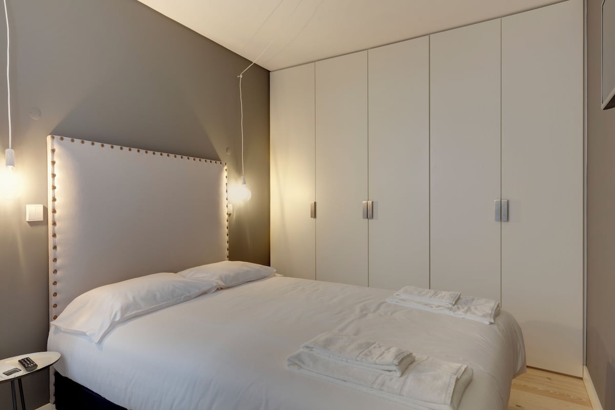 A modern bedroom with a large bed, bedside tables, and a wardrobe.