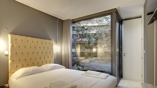 A bedroom with a large bed, a wooden headboard, and a view of greenery through a sliding glass door. - City Stays Bica Apartments (Lisbon)