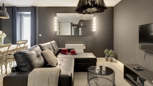 A modern living room with a sectional sofa, a round coffee table, a large mirror, and a flat-screen TV. - City Stays Bica Apartments (Lisbon)