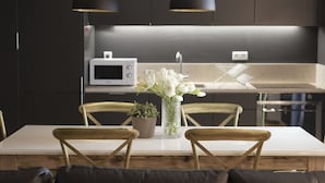A modern kitchen with dark cabinetry, a white countertop, a microwave, and a vase with white flowers. - City Stays Bica Apartments (Lisbon)