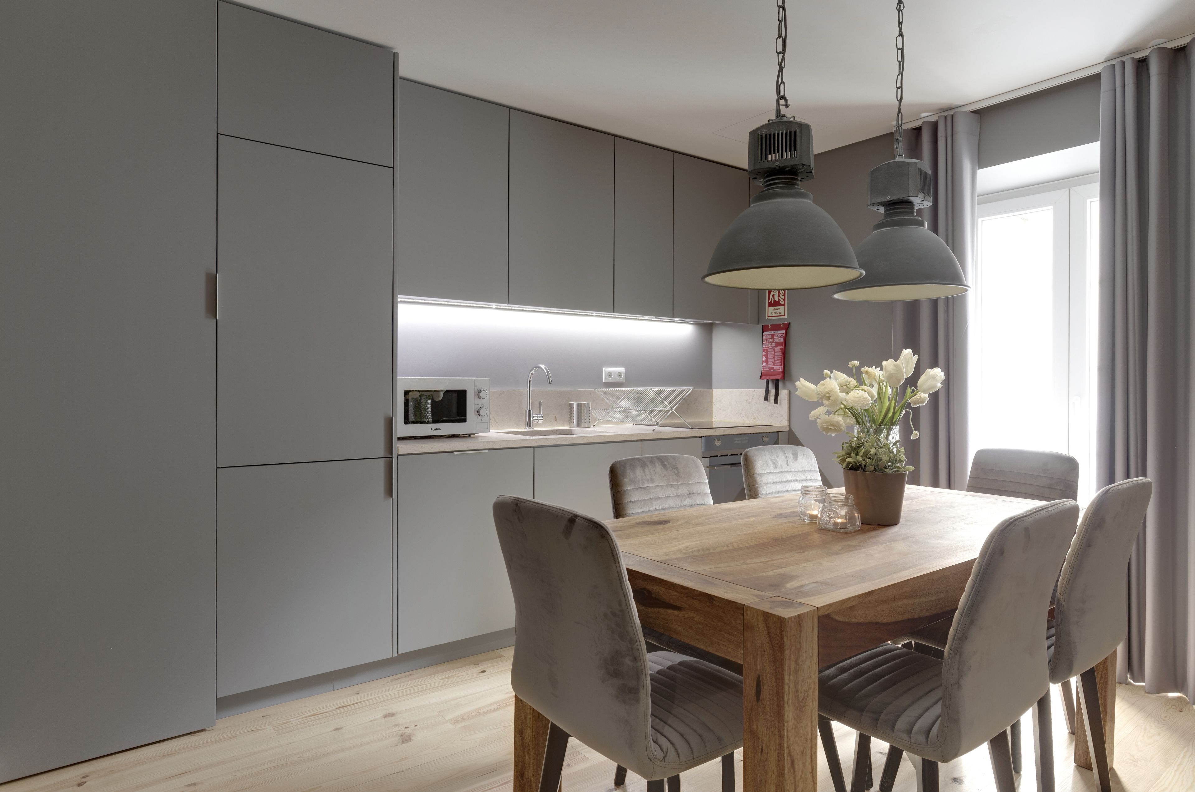 A modern kitchen with grey cabinets, a wooden dining table, and two pendant lights.