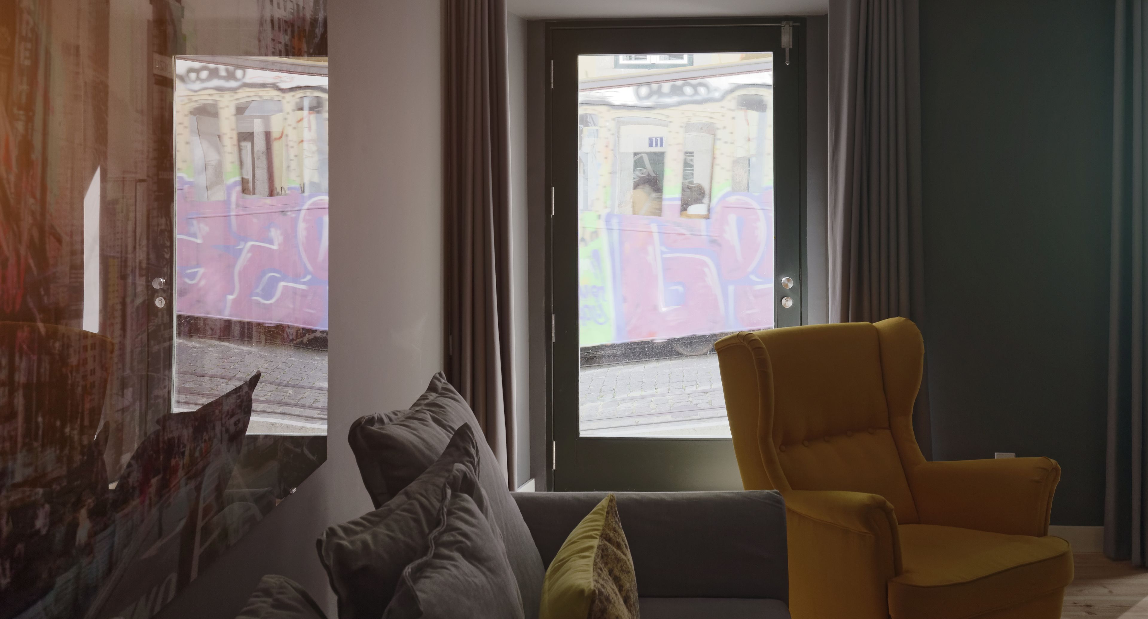 A room with a sofa, a yellow armchair, and a view of a street with graffiti.