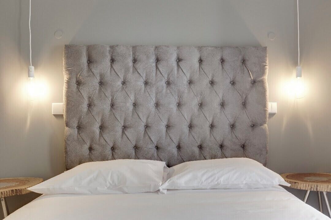 Ein Bett mit einem durchgestopften Kopfteil, zwei Nachttische und Wandleuchten.