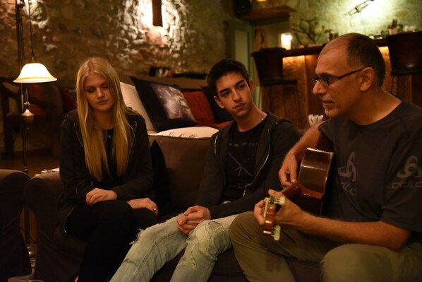 Three people sitting on a couch in a dimly lit room with a stone wall and a hanging lamp. - Pritanio (Sparta)