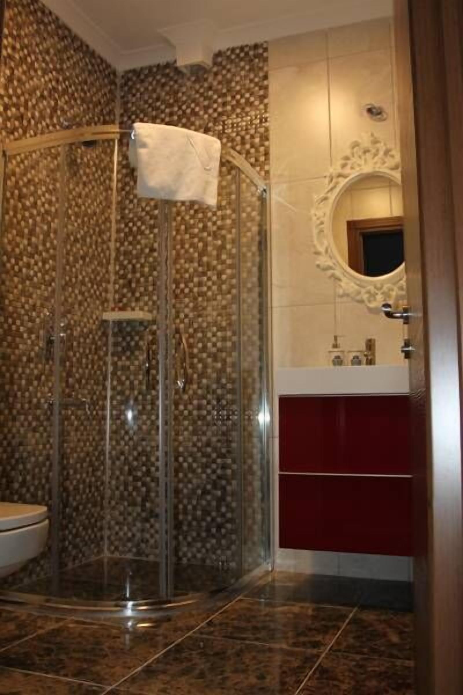 Un baño con ducha cubierta por vidrio, tocador rojo y espejo con marco decorativo.
