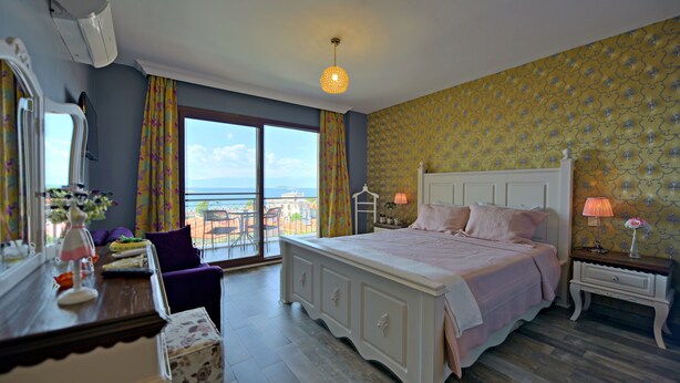 A bedroom with a large bed, a dresser, a vanity, and a view of the sea. - Nilufer Otel - Adult Only (Ayvalik)
