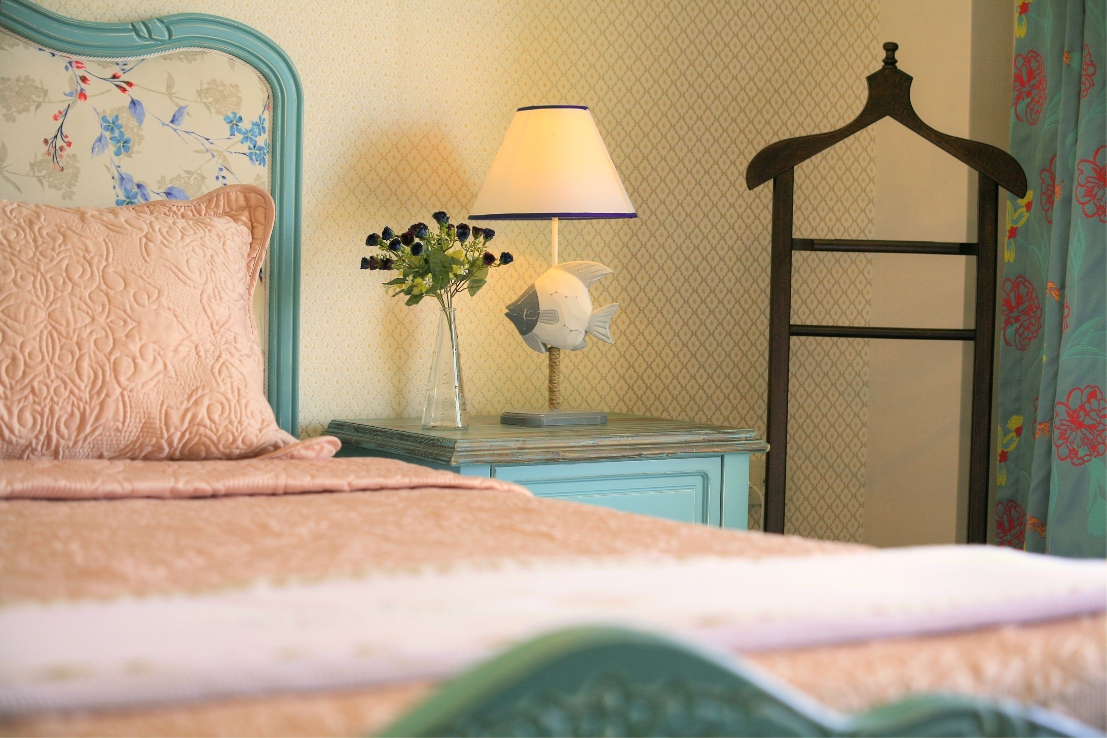 A neatly made bed with a pink pillow and a blue nightstand beside it.
