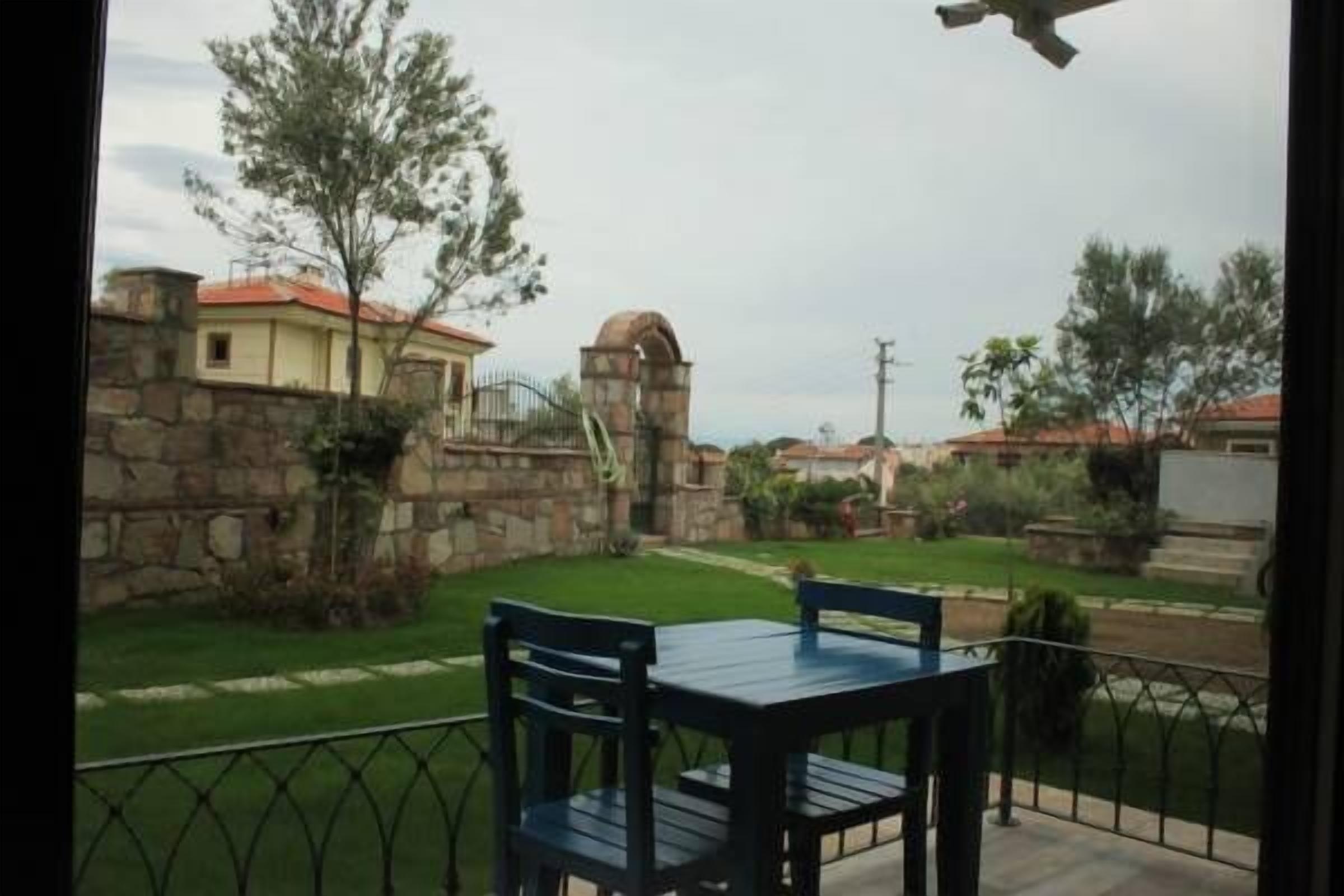 A balcony with a table and chairs, a stone wall, and a view of a residential area with houses and greenery.