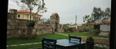A balcony with a table and chairs, a stone wall, and a view of a residential area with houses and greenery.